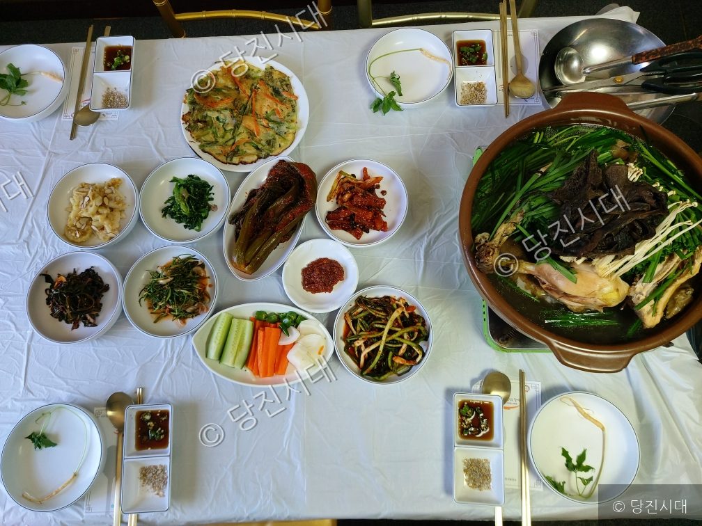 식탁 위에 능이닭백숙과 다양한 밑반찬이 차려져 있다.