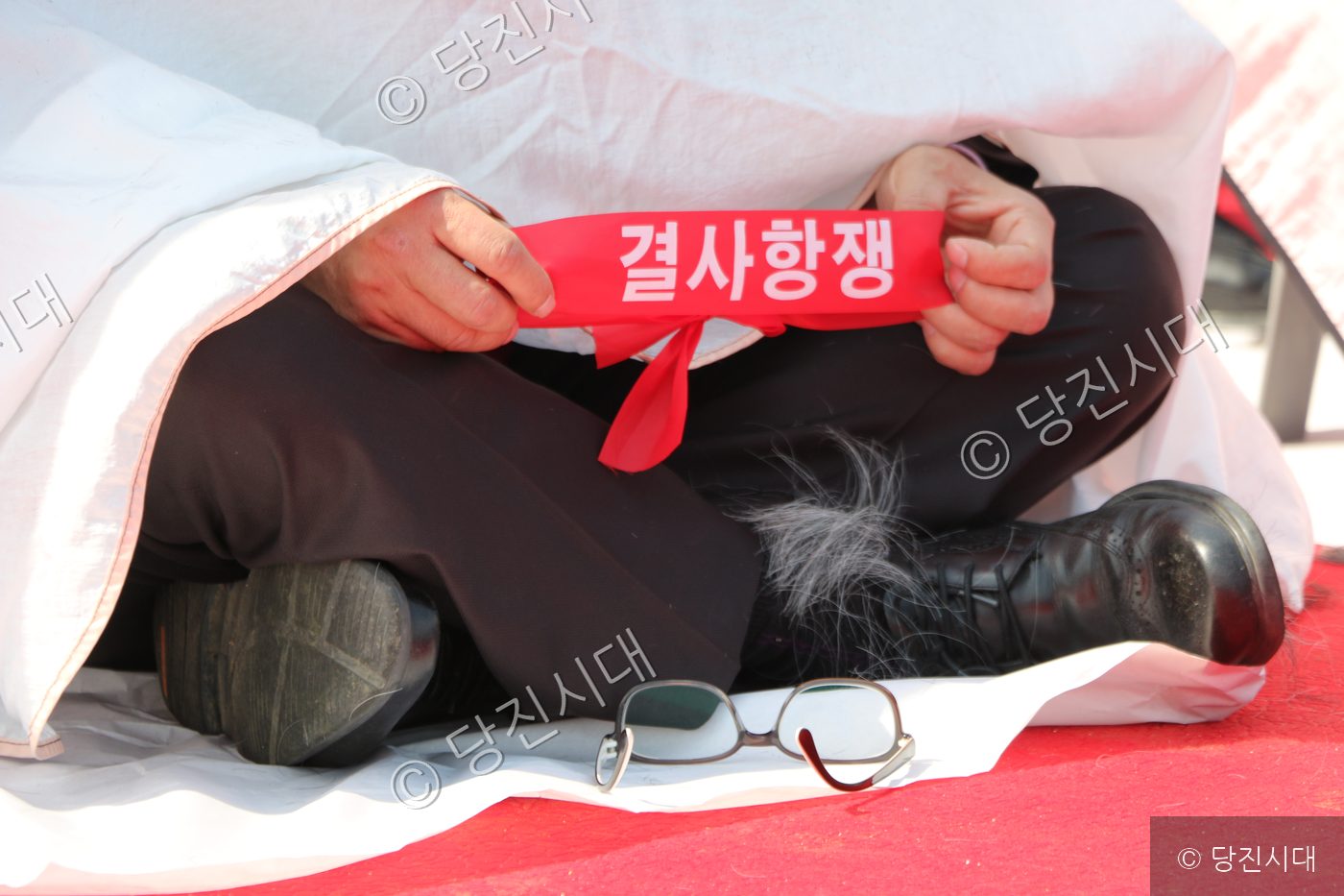 결사항쟁이 적힌 붉은 띠를 들고 앉아 있는 모습