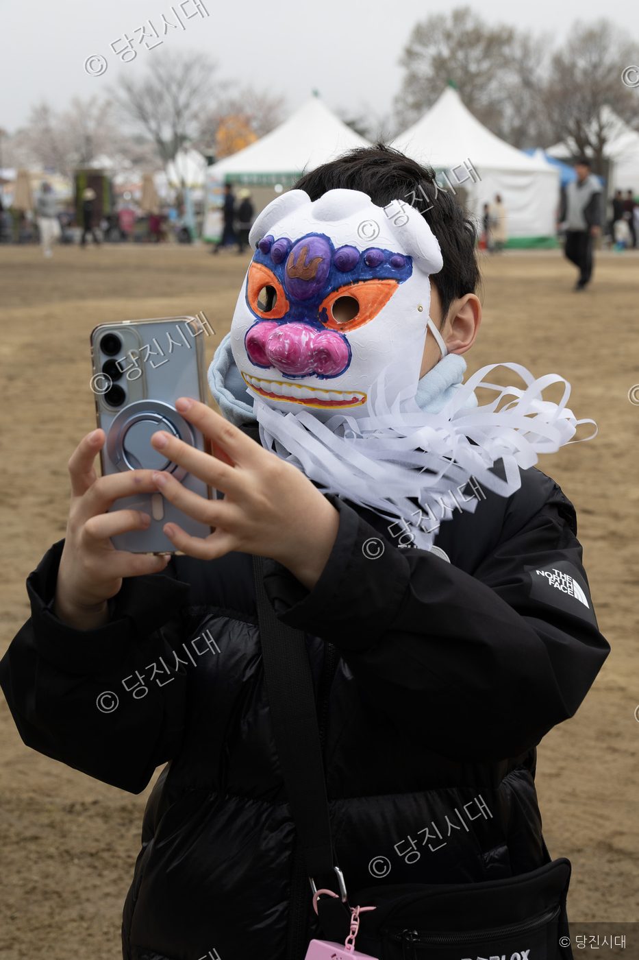기지시줄다리기 축제에서 한 어린이가 탈을 쓰고 스마트폰으로 사진을 찍고 있다.