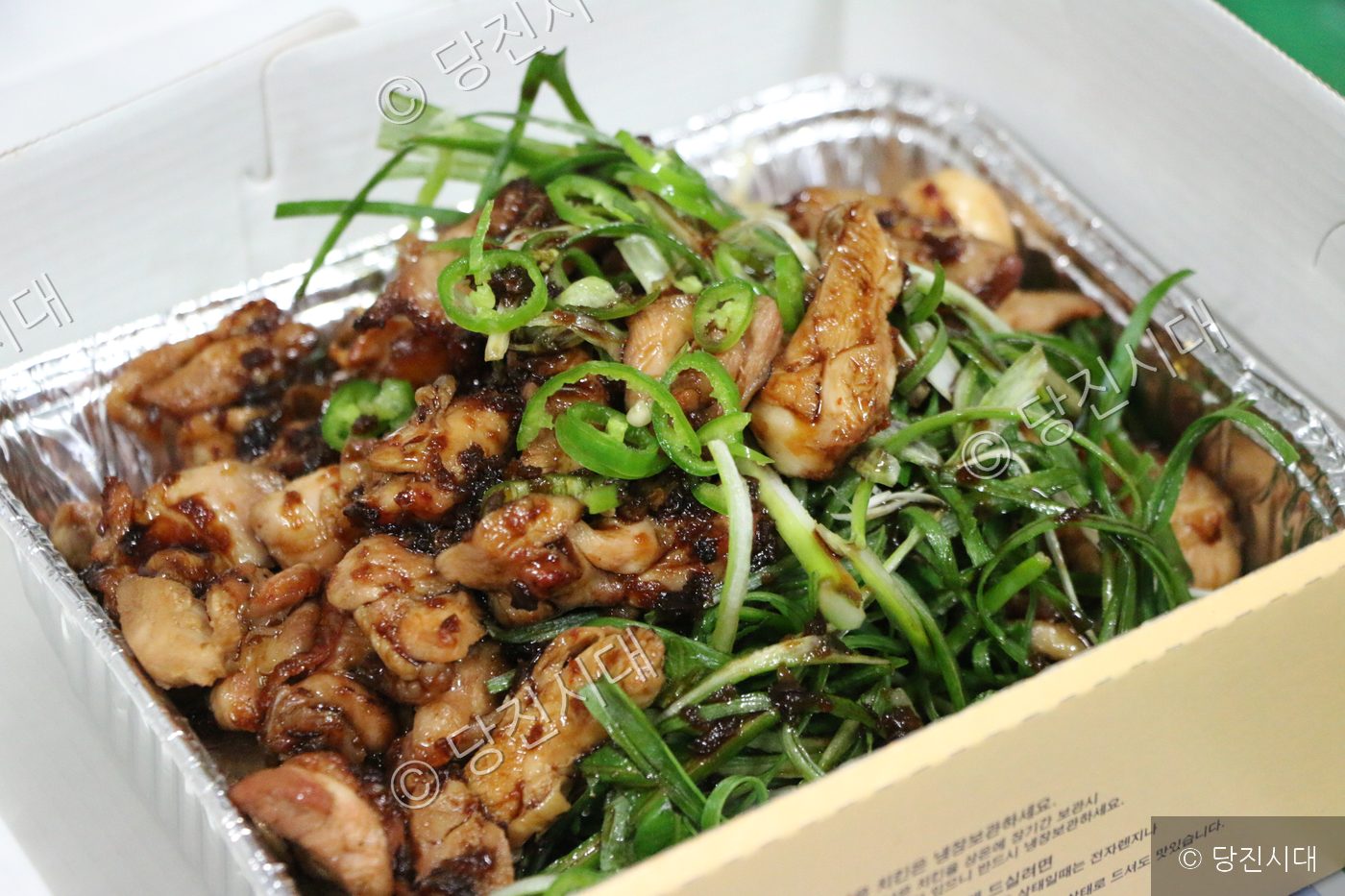 은박 용기에 담긴 양념 치킨과 파채가 놓여 있다.