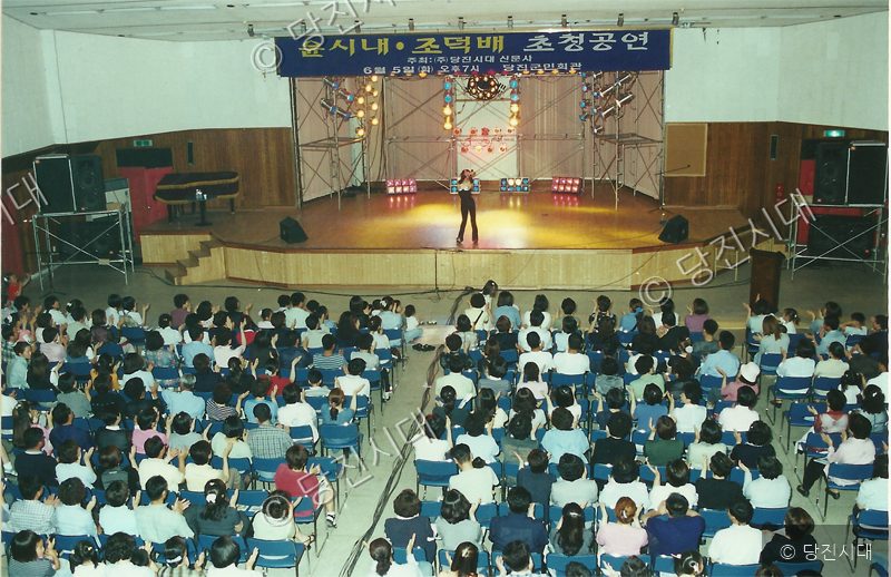 실내 공연장에서 관객들이 가수의 무대를 관람하고 있다.