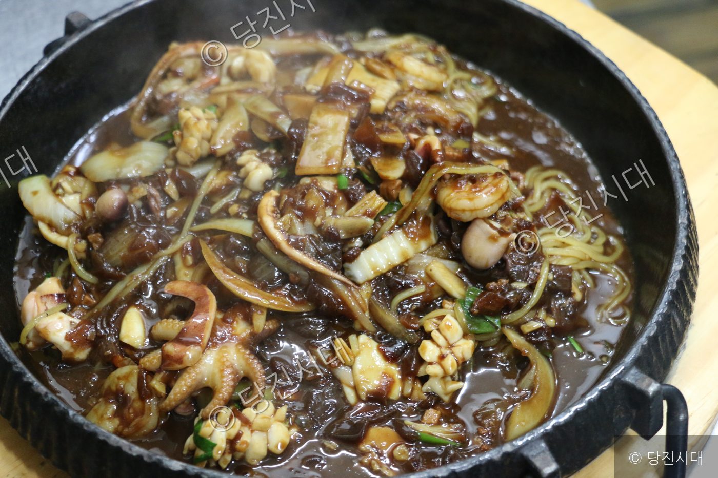 검은 철판 그릇에 담긴 해물 짜장면이 조리되어 있다.