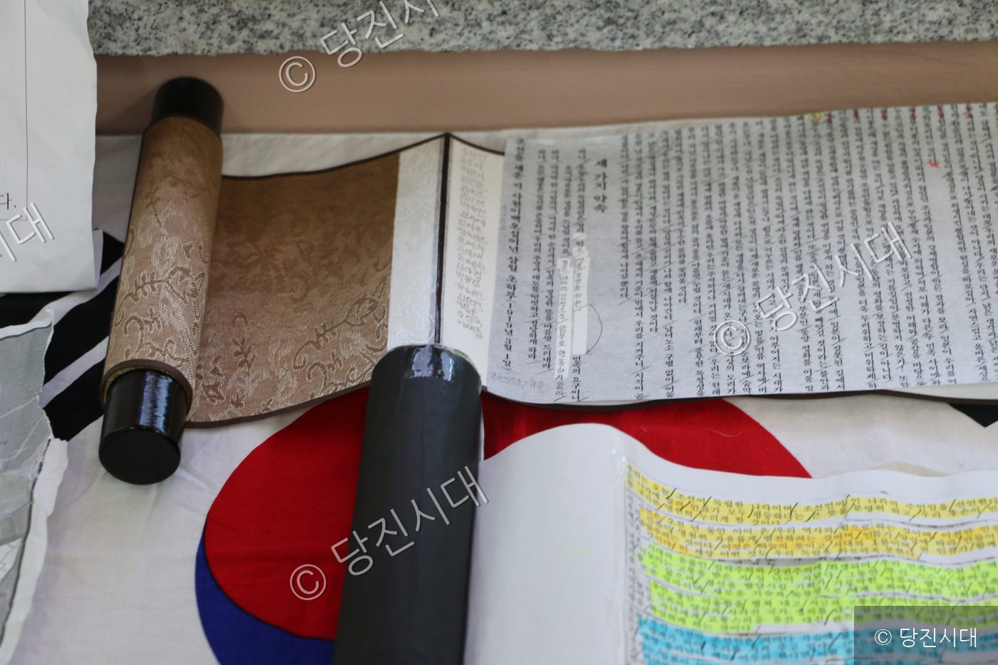 태극기 위에 펼쳐진 독립선언서와 붓글씨 두루마리가 놓여 있다.