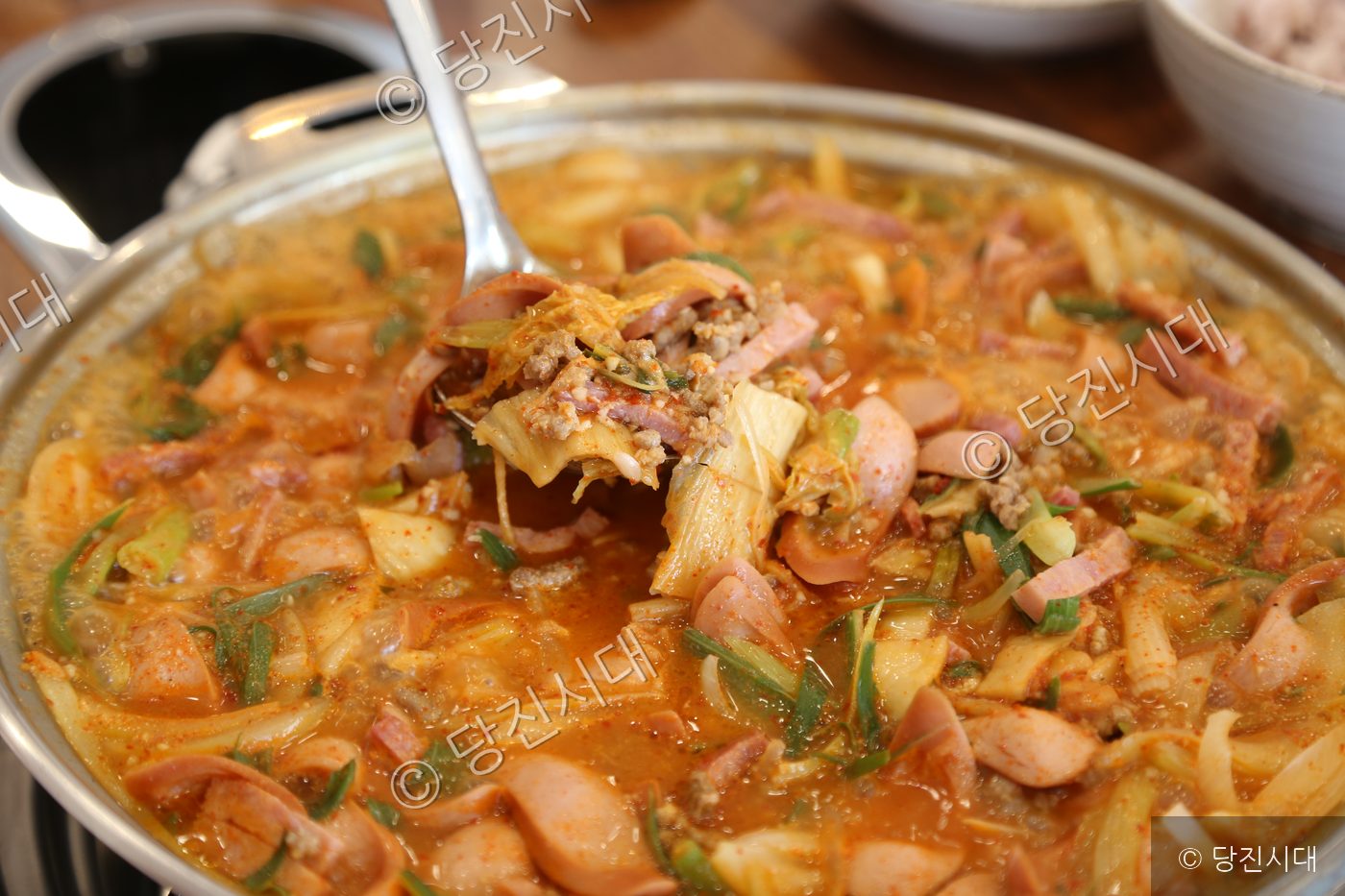 김치와 햄이 듬뿍 담긴 송탄 부대찌개를 국자로 떠서 보여주고 있다.