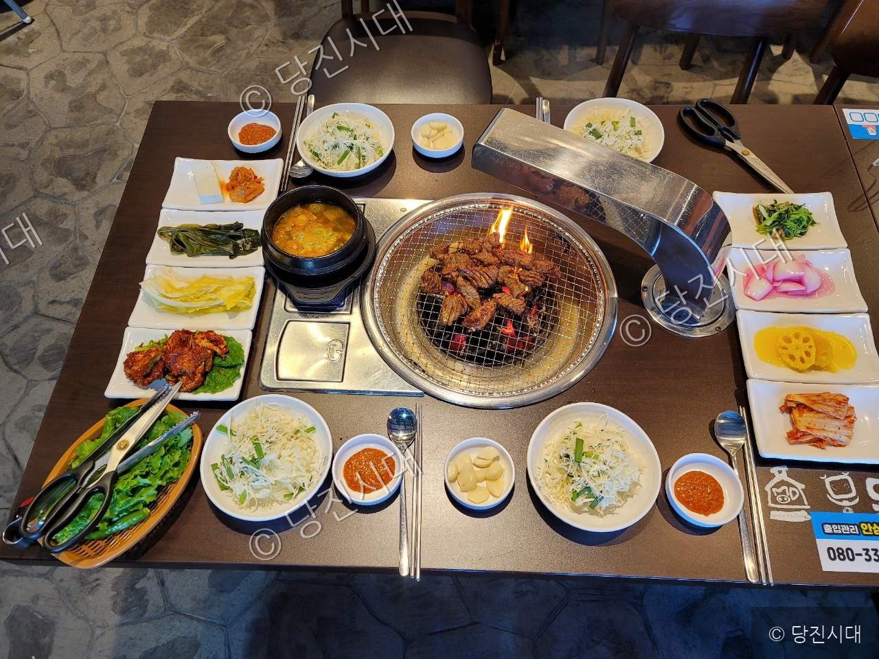 식당 테이블 위에 숯불구이와 다양한 밑반찬이 차려져 있다.