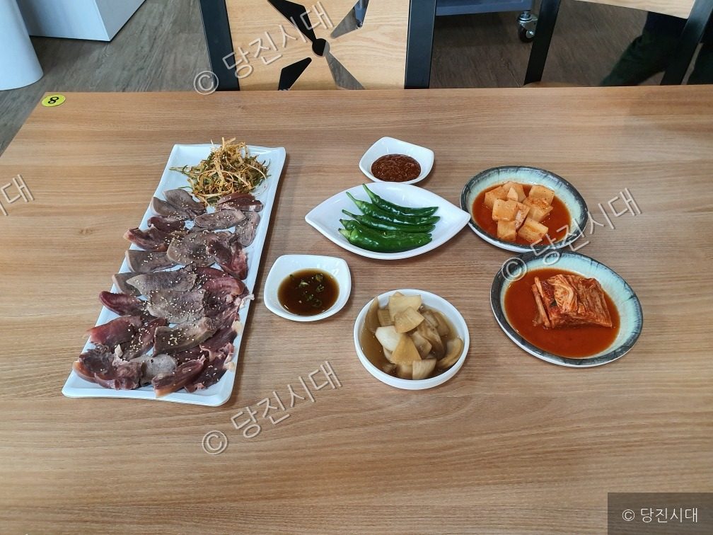 식당 테이블 위에 소머리국밥 고기 수육과 다양한 밑반찬이 차려져 있다.